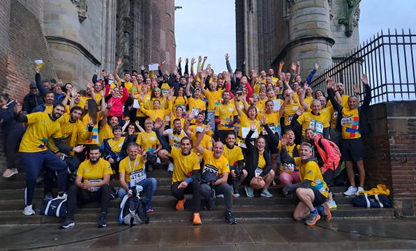 Groupe de participants en tenue TeamSportLaPoste rassemblés sur les marches d’un bâtiment en pierre après une course.