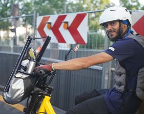 Conducteur de véhicule utilitaire léger à deux roues portant un casque, stationné devant des panneaux de signalisation sur une zone de circulation sécurisée.